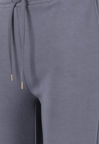 Grå joggingbyxor i mjukt tyg, med resårmidja och dragsko med gyllene detaljer, slät yta och slim fit.