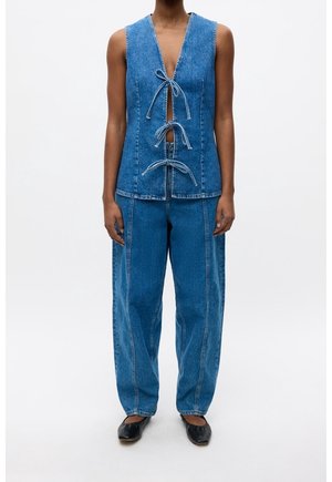 Veste en denim avec un décolleté en V profond et des liens à l'avant, associée à un pantalon en denim ample à taille haute. Les deux pièces sont en bleu moyen avec des coutures contrastées.