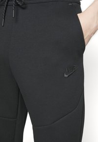 Joggers neri Nike con una texture morbida, dotati di una vestibilità slim, tasca laterale e un logo tono su tono sulla coscia destra.