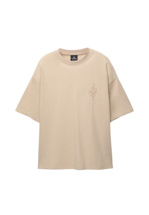 Beige übergroßes T-Shirt aus Baumwolle mit rundem Ausschnitt und kurzen Ärmeln. Enthält ein gesticktes Blätterdesign auf der linken Brust.