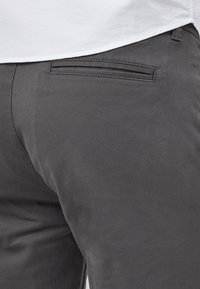 Pantalon gris à la texture lisse, avec une poche arrière unique et des détails cousus près de la taille.