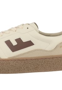 Sneaker w kolorze kremowym z brązowym logo, teksturowaną podeszwą środkową i gładką skórzaną cholewką. Posiada płaskie sznurówki oraz zaokrąglony kształt palców.