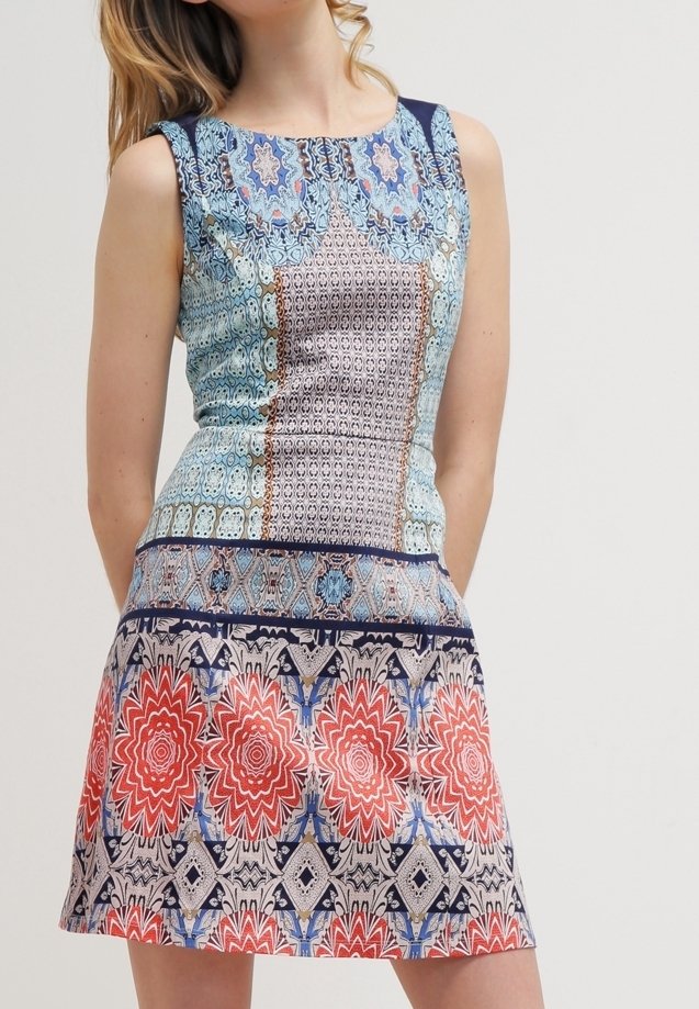Šaty bez rukávů s modrou vzorovanou korzetovou částí s geometrickými motivy, přecházející do sukně s velkými červenými květinovými vzory na světlém pozadí.