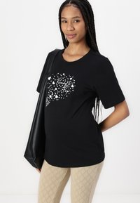 Svart bomull t-skjorte med korte ermer, med hvitt grafisk design av hjerter og teksten "Ready to Pop." Båret med mønstrede beige leggings.