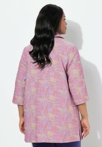 Mehrfarbige, gemusterte Jacke mit lockerer Passform, Dreiviertelärmeln und seitlichen Schlitzen, die in Pink-, Lila- und Gelbtönen gestaltet ist.
