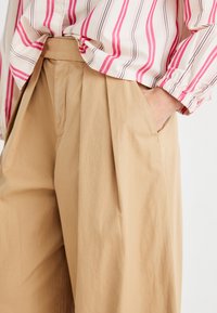 Beiga veckade byxor gjorda av lättviktsmaterial med sidfickor, kombinerade med en randig blus i vitt och rosa nyanser.