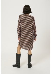 Langärmliges, gemustertes Kleid mit geometrischem Design in Rosa und Braun, lockere Passform und seitlichen Schlitzen. Kombiniert mit knielangen schwarzen Stiefeln.