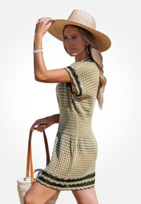 Strickkleid in Olivgrün mit offenem Netzdesign, schwarzem Spitzenbesatz am Saum, kurzen Ärmeln, kombiniert mit einem Strohhut und einer geflochtenen Handtasche.