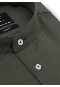 Slim fit koszula z ciemnooliwkowej bawełny. Posiada wąski kołnierzyk, pojedyncze zapięcie na biały guzik oraz przeszycia wzdłuż krawędzi.