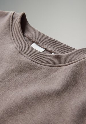 Brun sweatshirt med ribbet rund hals, blød stoftekstu. Lille hvidt mærke ved kraven. Glat overflade med minimale detaljer.