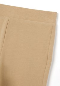 Joggers in misto cotone beige con vita elasticizzata e tasche laterali. Texture liscia, design aderente e bordi puliti.