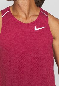 Rotes, athletisches Tanktop aus strukturiertem Stoff, mit Rundhalskragen, perforiertem Design und einem weißen Nike-Logo auf der Brust.