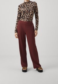 Långärmad tröja med leopardmönster i kombination med höga burgundy vida byxor. Tillbehören inkluderar plattformssandaler med tjock sula.