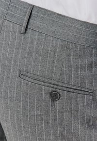 Szare spodnie w paski z pojedynczą tylną kieszenią z czarnym guzikiem, talią dostosowaną do figury oraz gładkim materiałem.