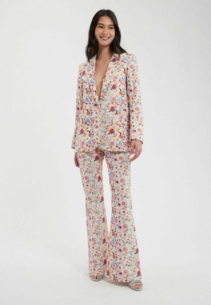 Costume floral avec des motifs rose, bleu et jaune. Le blazer a un col cranté. Le pantalon est évasé en bas. Tissu léger.