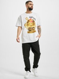 Valge T-särk, millel on graafika näo ja burgeriga, koos mustade cargo-pükstega ja valgete tennisetossudega. Lihtne ja mugav disain.