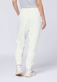 Weiße Jogginghose mit gerippten Bündchen und Bund, die einen lässigen Schnitt und eine weiche Textur aufweist. Getragen mit hell gefärbten Sportschuhen.