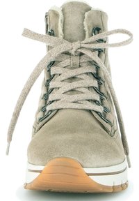 Beige velúr csizma műszőrme béléssel, fűzős kialakítással, fekete szemcsavarokkal és texturált gumi talppal. A frontális nézet kiemeli a részleteket és a formát.
