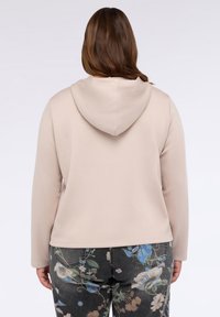 Hanorac bej cu un design ajustat și o textură moale, asortat cu blugi închiși la culoare cu un model floral în nuanțe de albastru și crem.