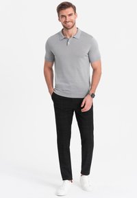 Polo shirt gris à manches courtes avec col côtelé, associé à un pantalon slim-fit à carreaux noirs et des baskets blanches. Tenue décontractée.