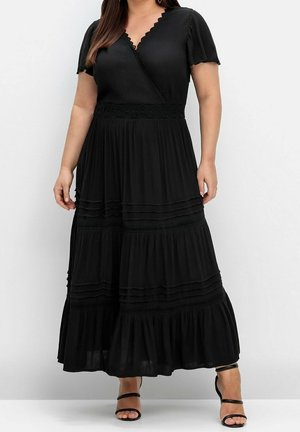 Woman wearing a black, short-sleeve, V-neck maxi dress with tiered ruffles and lace details, paired with black strappy high heels.