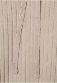 Tessuto a maglia beige con texture a coste verticali, corde sottili, finitura leggermente pelosa e una leggera lucentezza sulla superficie.