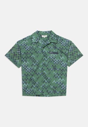 Chemise verte à manches courtes avec motif en zigzag dans des nuances de bleu et de noir, dotée d'une poche avant et d'un col.