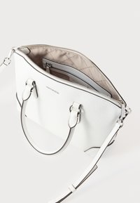 Λευκή δερμάτινη τσάντα χειρός με λεία υφή, δύο λαβές, αποσπώμενο λουράκι και φερμουάρ στο πάνω μέρος. Το εσωτερικό διαθέτει μια τσέπη και επένδυση.