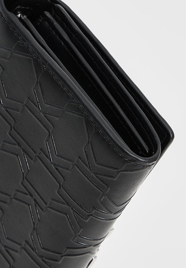Portefeuille en cuir noir avec un motif géométrique en relief, design plié et texture lisse et brillante avec coutures visibles.
