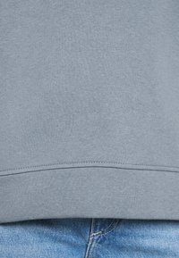 Ljusblå sweatshirt med en mjuk bomullstextur, rund halsringning och ribbad fåll, matchad med ljusblå denimjeans.