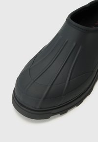 Black rubber slip-on shoe with a textured design and ridged detailing on the upper, featuring a thick, durable sole.