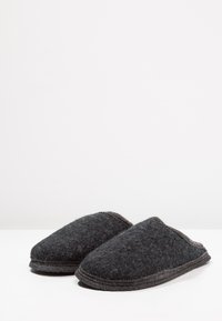 Grijze gevoelslippers met een ronde neus en ergonomisch ontwerp, met een getextureerd oppervlak en contrasterende donkergrijze stiksels langs de randen.