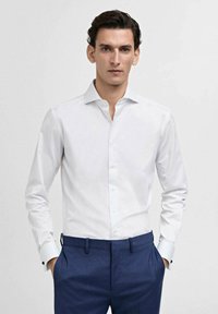 Weißes Hemd mit Spread-Kragen, langen Ärmeln und kontrastierenden blauen Manschetten, getragen mit dunkelblauen Hosen. Glatter, knitterfreier Stoff.
