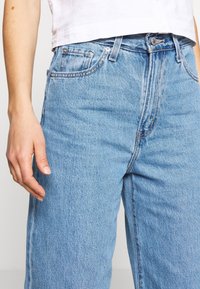 Světle modré široké džíny s vysokým pasem, pěti kapsami a viditelnými švy, vyjadřující klasický design a strukturu.