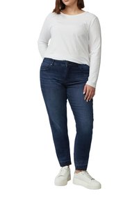 Dunkelblaue Jeans mit geradem Bein und leichtem Schmalverlauf, kombiniert mit einem weißen Langarmshirt und weißen Sneakern.