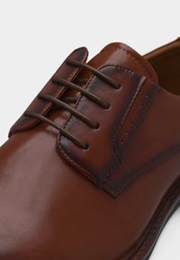 Κοντινό πλάνο καφέ δερμάτινου παπουτσιού φόρεμα με σκούρα καφέ κορδόνια και γυαλισμένες ραφές σε λευκό φόντο.