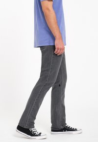 Pantalones de mezclilla gris con un corte recto, que presentan un agujero desgastado. Combinados con zapatillas negras y una camiseta de color azul claro.