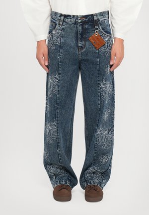 Blue denim wide-leg jeans with white floral embroidery on both sides, featuring a high waist and a brown tag attached.