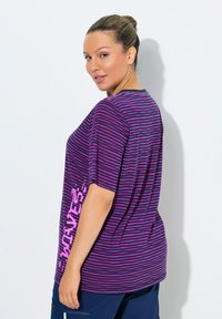 Camiseta de manga corta con rayas púrpuras y rosas, que presenta un estampado gráfico en el lateral, con un ajuste holgado y una textura de tela suave.