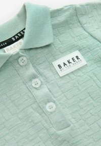 Lys grøn, tekstureret polo-shirt med et vævet mønster, tre klare knapper og et rektangulært mærke med "BAKER" branding.