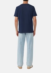 Granatowa bawełniana koszulka z okrągłym dekoltem, w zestawie z jasnoniebieskimi spodniami o szerokich nogawkach i beżowymi butami. Styl minimalistyczny, bez widocznych wzorów.