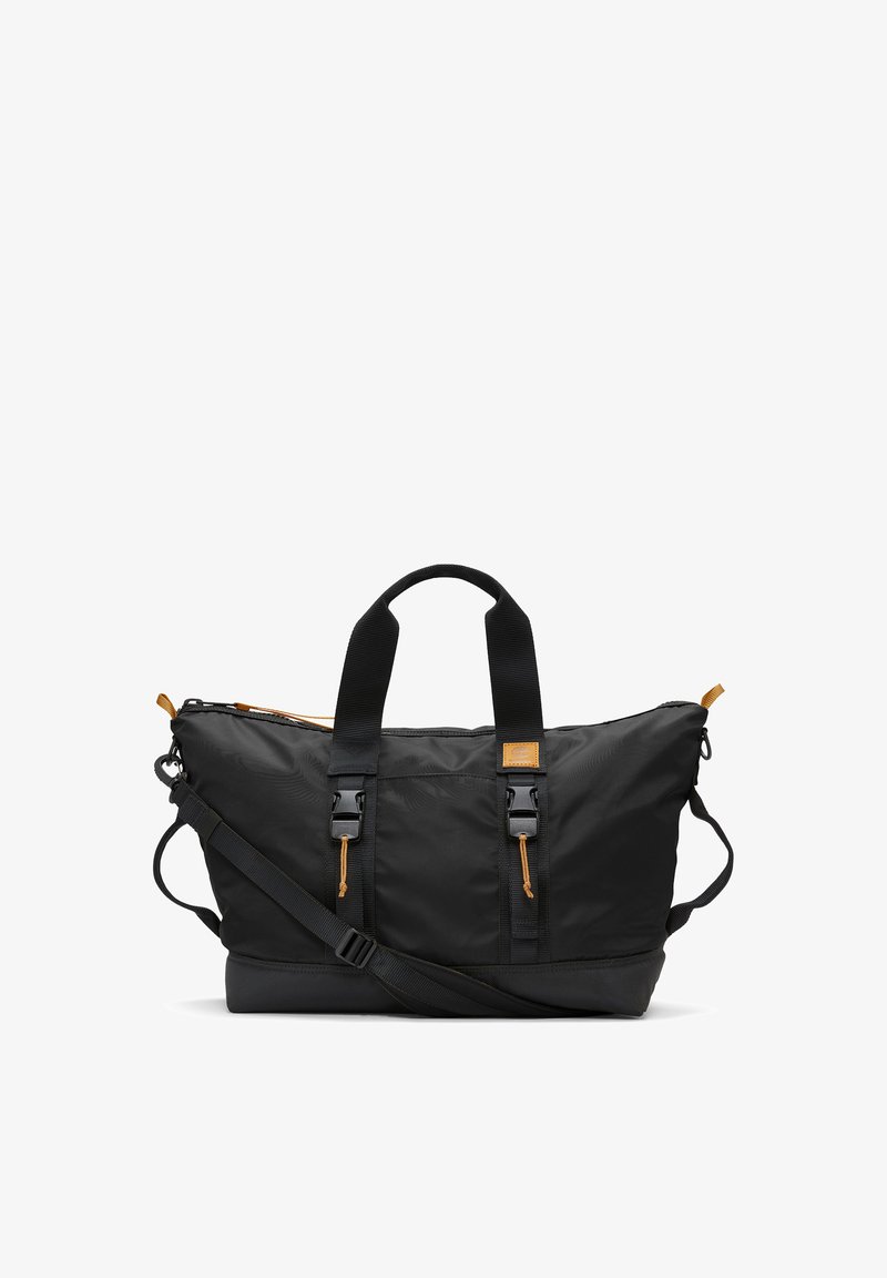 Černý nylonový cestovní kufr s hnědými koženými akcenty, dvojitými horními madly, nastavitelným ramenním popruhem a zipovým uzávěrem. Obsahuje boční kapsy.