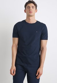 Camiseta de manga corta azul marino hecha de algodón, con cuello redondo y pequeño logo bordado en rojo, blanco y azul en el pecho.