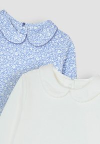 Két galléros blúz: az egyik világoskék, fehér virágmintával, a másik pedig sima fehér. Mindkettő kerek gallérral és gombos záródással rendelkezik.