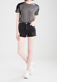 Camiseta gris con detalle floral negro en los hombros, combinada con shorts de mezclilla negra desgastados y zapatillas deportivas blancas.