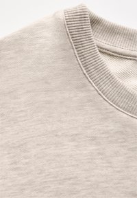 Close-up van een beige sweatshirt met ronde hals waarin de geribbelde kraag en de textuur van de gebreide stof zichtbaar zijn.