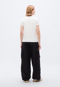 Άσπρο εφαρμοστό t-shirt και μαύρο cargo παντελόνι με πλατείς ρεβέρ και πλευρικές τσέπες. Μαλακό ύφασμα, μινιμαλιστικός σχεδιασμός και άνετη εφαρμογή.