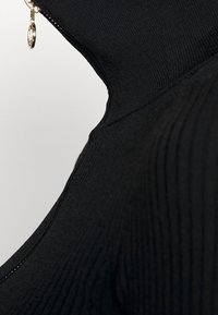 Zwart gebreid kledingstuk met een hoge kraag en een ritssluiting. De textuur heeft verticale ribbels, met een glanzende ritstrekker als accent.