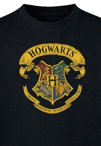 Must have must kunst must. T-särk, millel on värviline Hogwarts'i embleem, kus on lõvi, madu, mäger ja kotkas, ümbritsetud kollase riba ja ladina keeles tekstiga.