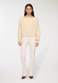 Kremowy krótki sweatshirt z szerokim dekoltem i długimi rękawami, w zestawieniu z jasnobeżowymi spodniami o prostych nogawkach. Brązowe czółenka z wysmuklającym czubkiem.